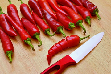 line fresh cayenne red hot chili peppers with sharp kitchen knife on wooden table