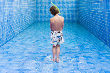 Boy stands in an empty blue swimming pool waiting for the water level to rise
