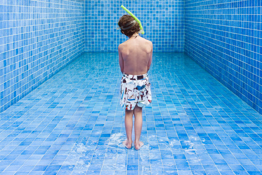 Boy stands in an empty blue swimming pool waiting for the water level to rise