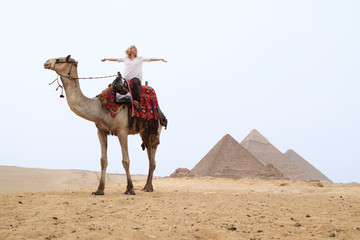 Frau auf Kamel breitet die Arme vor Freude aus vor den Pyramiden