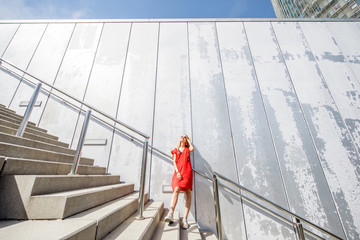 Business woman in red dress on the big stairway on the grey wall background