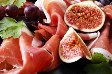 prosciutto with parsley, figs and grapes on a black stone food tray.