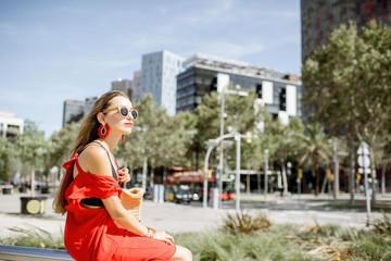 Lifestyle portrait of a woman in red dress sitting outdoors at the modern office district in Barcelona city