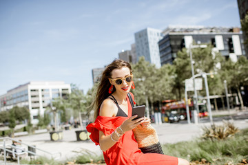 Lifestyle portrait of a business woman with phone in red dress sitting outdoors at the modern office district in Barcelona city