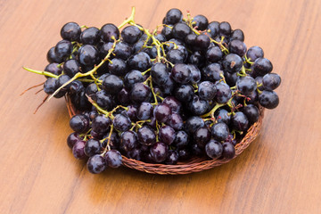 Ripe grapes in wicker basket on wooden table