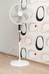 A white electric fan stands in a spacious room and cools the air
