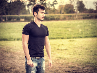 Attractive, fit young man relaxing standing on lawn in the countryside in the grass, looking away