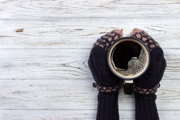 Female hands in mittens holding a cup of coffee on wooden background