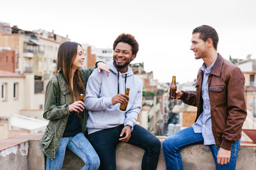 Portrait of happy young friends drinking bottles of beer on a rooftop.