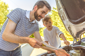 The boy and the father check the oil level in the car