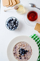 delicious, hearty and healthy breakfast, oatmeal on milk with berries - blackberries, blueberries, honey and black tea on a light background