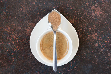 White espresso cup of coffee with a spoon of cinnamon on a dark brown background in Scandinavian style minimalism with a copy of the space view from above flat