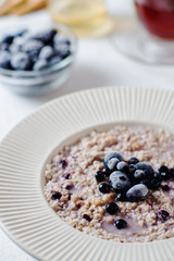 delicious, hearty and healthy breakfast, oatmeal on milk with berries - blackberries, blueberries, honey and black tea on a light background