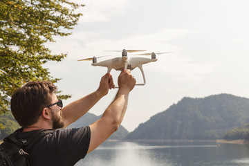 Man is holding white drone near Lake Vidraru at Fagaras Mountains. Romania