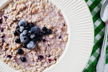 delicious, hearty and healthy breakfast, oatmeal on milk with berries - blackberries, blueberries, honey and black tea on a light background