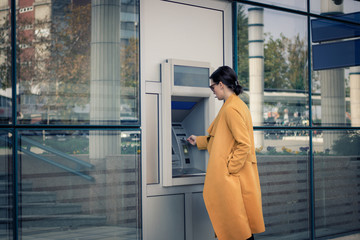 Young businesswoman using cash machine in front of bank.