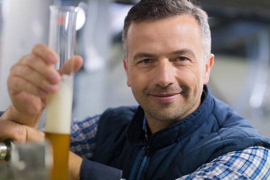 man looking at the beaker with beer in the factory
