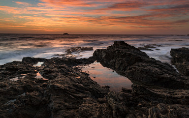 pink clouds reflected in a rock pool by the ocean