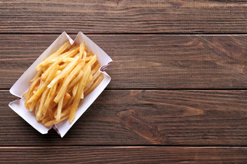 Paper container with yummy french fries on wooden table