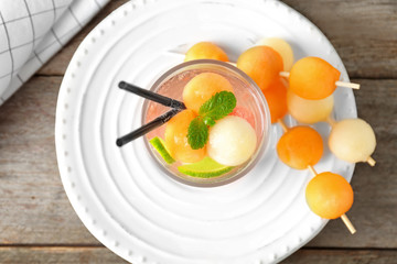 Glass of delicious cocktail with melon balls on plate