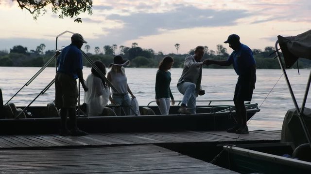 	 Men working in tourism industry helping tourists out of boat on the Zambezi