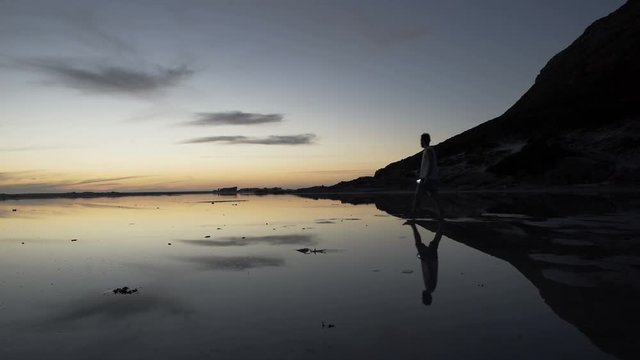  Man walking on beautiful sandy beach at sunset stops to take a photo of view