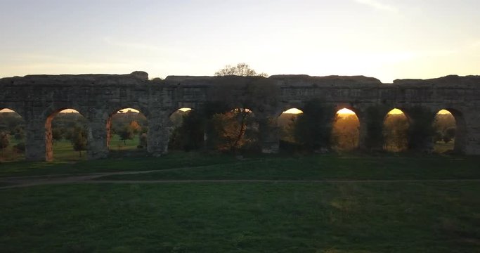 Video from above. Aerial view of the ancient Roman Aqueduct at sunset. Old ruins surrounded by a green public Park. Rome, Italy.