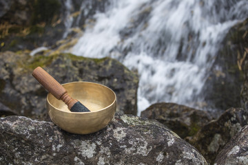 A Himalayan singing bowl on a rock with a waterfall in the background