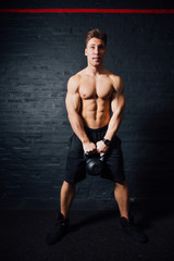 Fototapeta na wymiar Young muscular man training with kettlebells. man with naked torso on dark background.