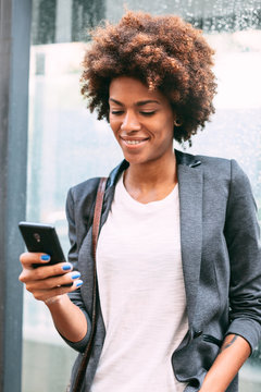 fro American businesswoman using phone in front a wet glass wall.