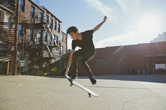 Backlit skateboarder doing a trick in a city lot