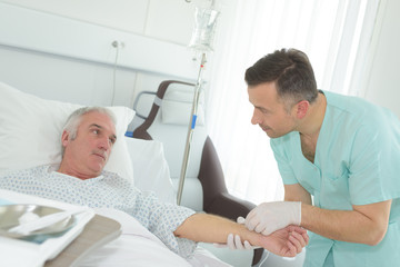 nurse inserting needle into arm of senior male hospital patient