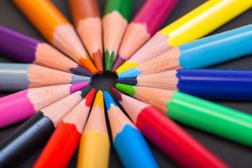 Naklejka premium Wooden color pencils on a black background. The tips of the pencils look in the center of the circle. The concept of creativity