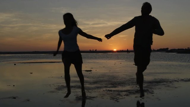  Romantic couple holding hands, running on beautiful sandy beach at sunset