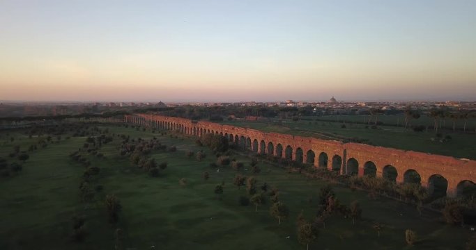 Video from above. Aerial view of the ancient Roman Aqueduct at sunset. Old ruins surrounded by a green public Park. Rome, Italy.