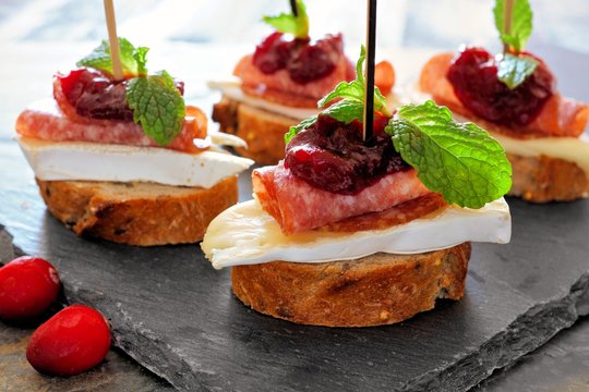 Holiday crostini appetizers with cranberry sauce, brie, salami, and mint close up on a slate server