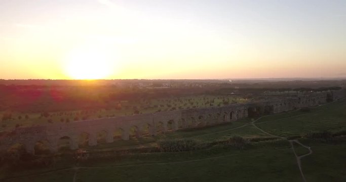 Video from above. Aerial view of the ancient Roman Aqueduct at sunset. Old ruins surrounded by a green public Park. Rome, Italy.