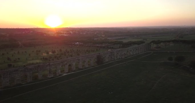 Video from above. Aerial view of the ancient Roman Aqueduct at sunset. Old ruins surrounded by a green public Park. Rome, Italy.