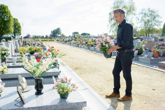 Man by graveside holding pot of flowers