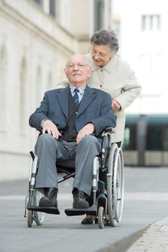 elderly wife pushing the husband on the wheelchair