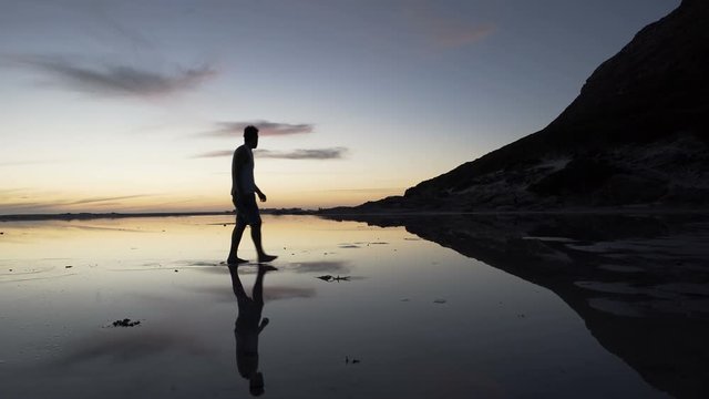  Man walking on beautiful sandy beach at sunset stops to take a photo of view