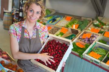 portrait of smiling female staff holding crate full of cherries