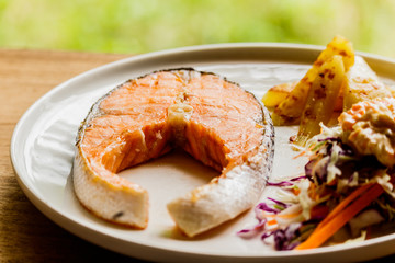 Salmon steak in a white plate on a wooden table.