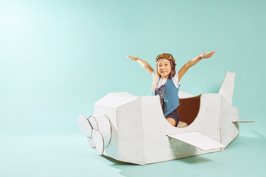Little cute girl playing with a cardboard airplane. White retro style cardboard airplane on mint green background . Childhood dream imagination concept .