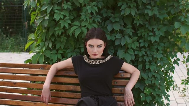 Sexy girl in long black dress and high heels sitting on a bench in the Park. Portrait of a sexy bitches on a Park bench.