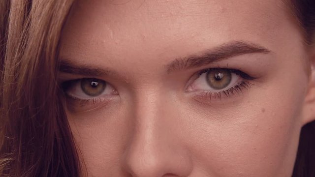 The girl looks intently into the camera, modestly closes her eyes, lowers her face down, embarrassed, modest. Close-up face of a beautiful cute girl. Bright makeup on the face, expressive green eyes.