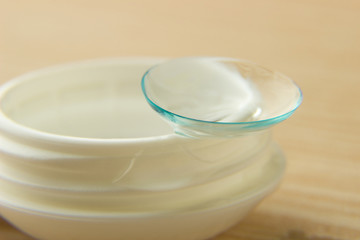Contact lenses for the eyes and a white container with a solution on a wooden table