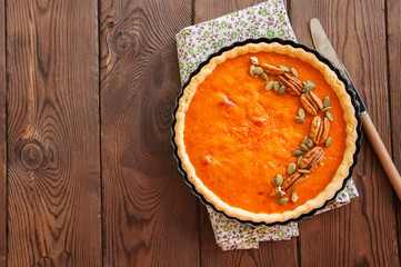 Pumpkin pie - traditional american dessert garnished with pecans and seeds on a wooden background