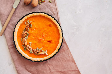 Traditional american baking - Pumpkin pie garnished with pecans and seeds on a white stone background