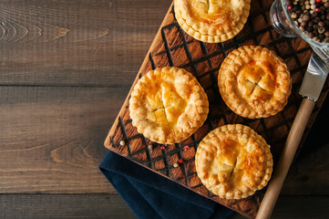 Mini meat pies from flaky dough on a wooden board over wooden background. © galiyahassan